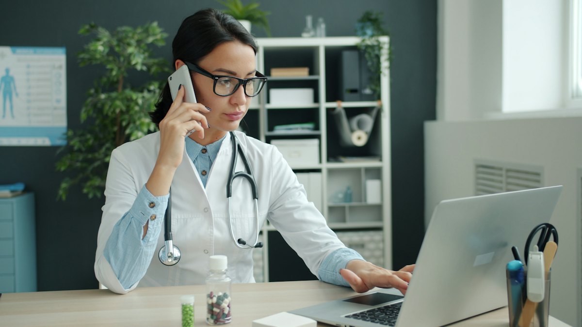 A healthcare professional on the phone while working on a laptop